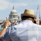 A man takes a photo of Millennium Bridge, with St Paul's Cathedral in the background.