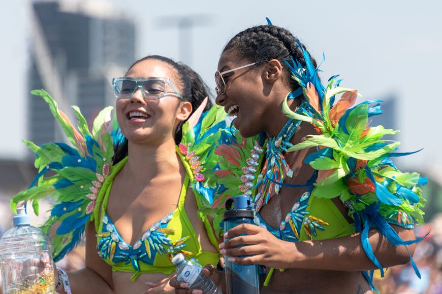 Two young women wearing bright green and blue feather-covered costumes smile at each other at an event in Toronto. 
