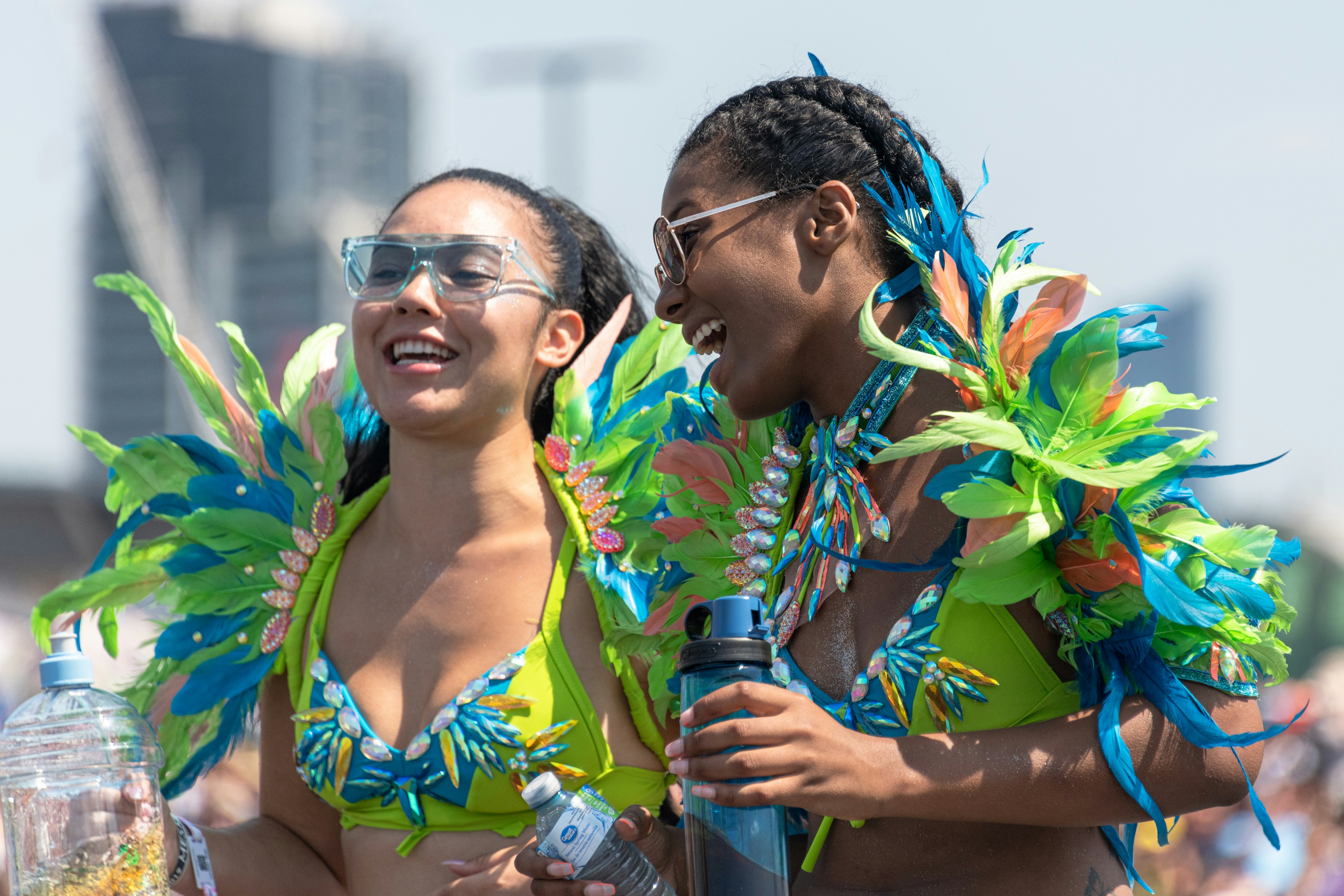 Two young women wearing bright green and blue feather-covered costumes smile at each other at an event in Toronto.