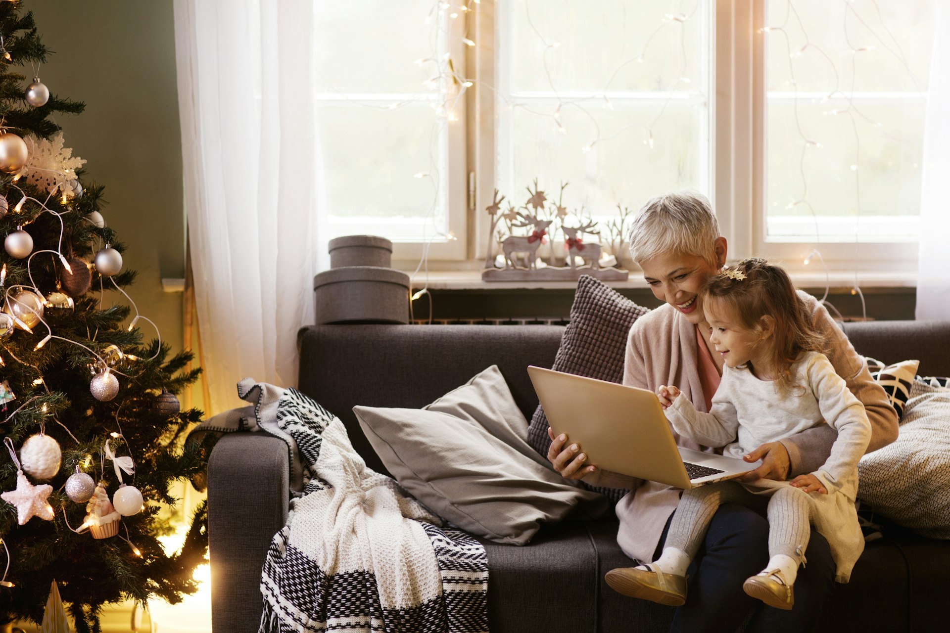 Happy grandmother and granddaughter using laptop while sitting on sofa 