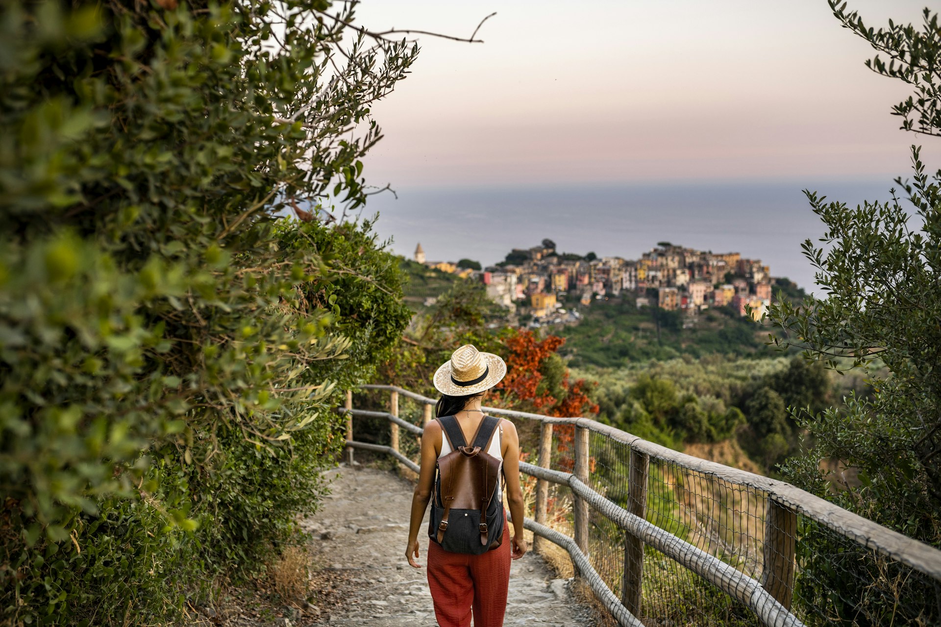 Female tourist wearing a straw hat, seen from behind walking towards Corniglia village, a beautiful town on the Cinque Terre coast
