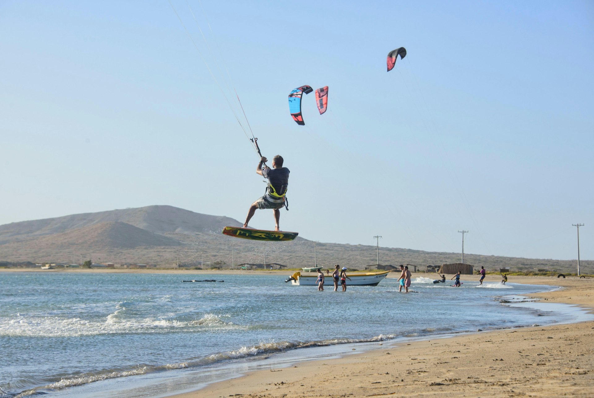 A kitesurfer on a board is lifted up above the sand and out to sea