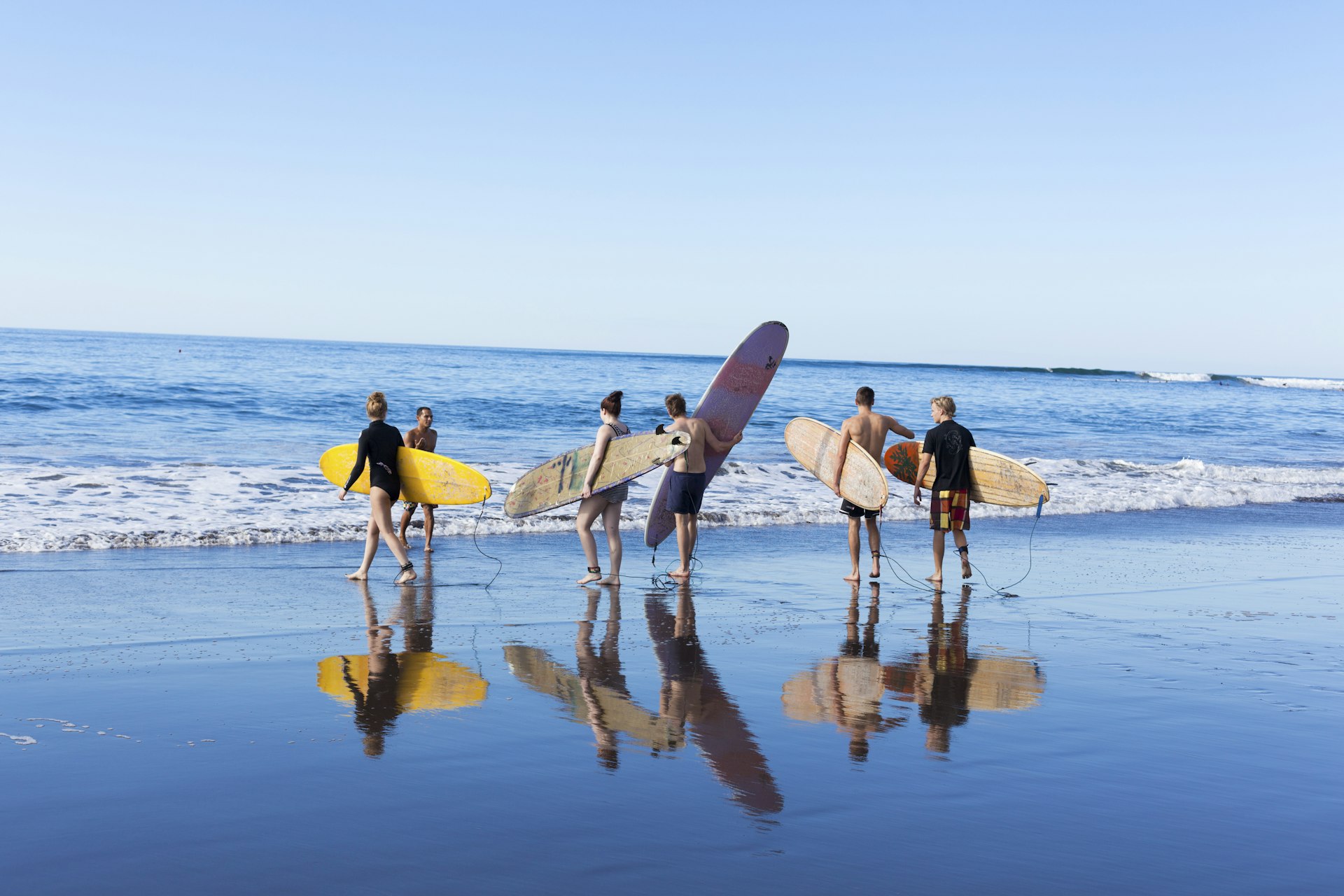 Tourist man and woman carrying a surf board and walking into the sea after finishing surf lesson in Playa El Tunco, El Salvador