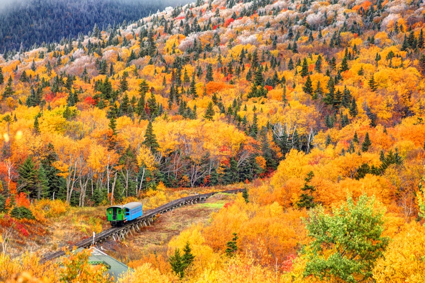 Cog railway train on Mt Washington in New Hampshire climbing through autumn foliage.