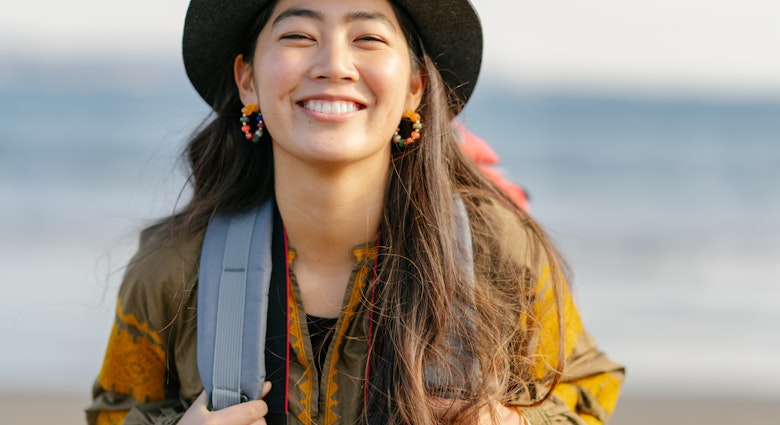 A close-up portait of a happy female solo traveller at the beach.