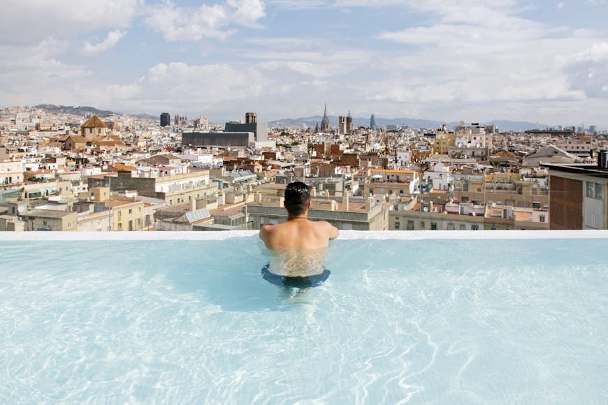 Rear view of a young man relaxing in the pool and looking at Barcelona city skyline