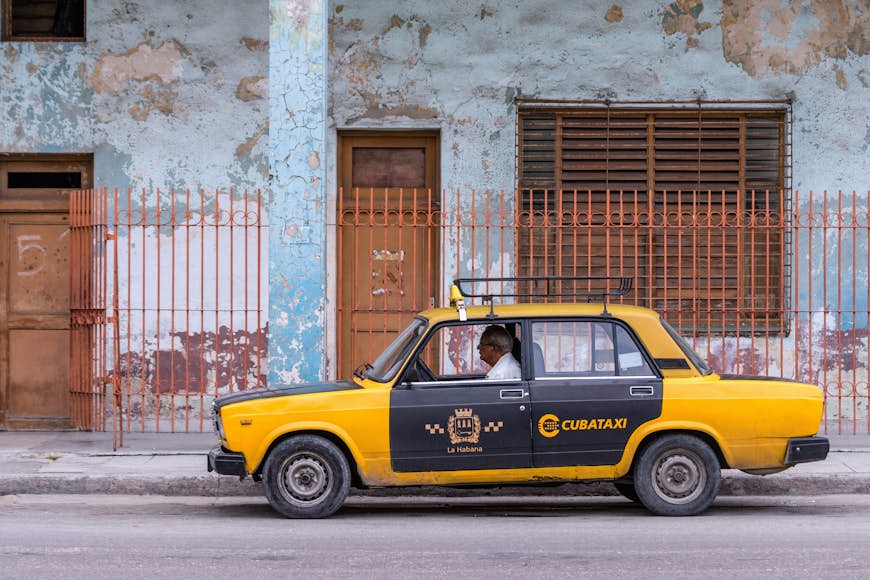 A black-and-yellow car parked outside a building with the word Cubataxi on the side