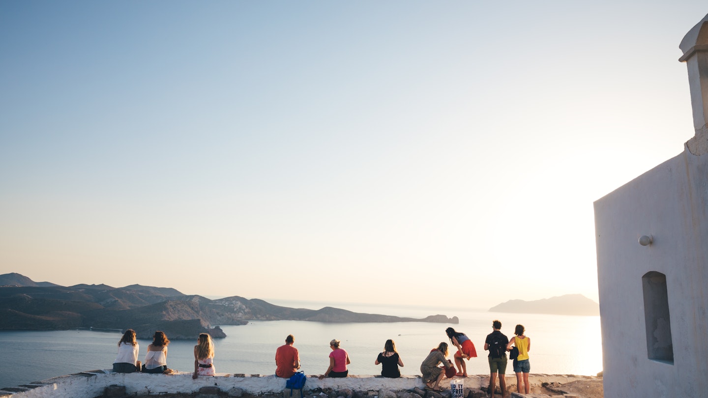 Milos island, Greece - June 12, 2018: Group of tourist sitting on top of the hill in Kastro to watch an amazing sunset. Kastro is the highest spot of Plaka, the capital of Milos.