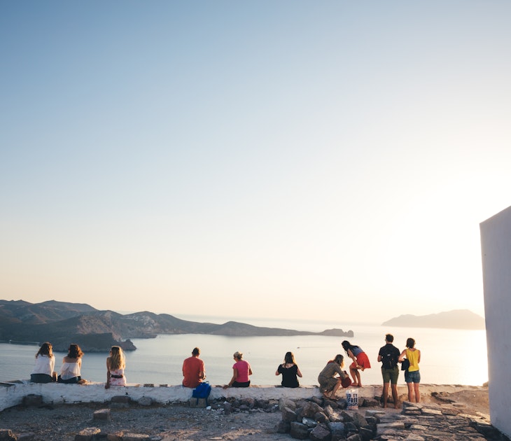 Milos island, Greece - June 12, 2018: Group of tourist sitting on top of the hill in Kastro to watch an amazing sunset. Kastro is the highest spot of Plaka, the capital of Milos.