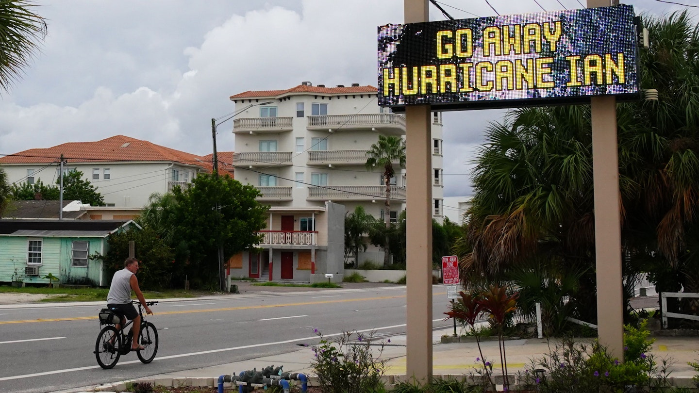 A man rides a bike past the message "Go Away Hurricane Ian" at a condominium complex in St. Pete Beach on September 27, 2022 in St. Petersburg. - The US National Hurricane Center (NHC) said Ian made landfall just southwest of the town of La Coloma, Cuba, at about 4:30 am local time (0830 GMT). The hurricane was packing maximum sustained winds of 125 miles (205 kilometers) per hour, the NHC said, making it a Category 3 storm on the Saffir-Simpson scale. (Photo by Bryan R. Smith / AFP) (Photo by BRYAN R. SMITH/AFP via Getty Images)