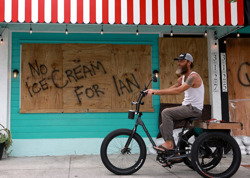 A bicyclist rides past a sign reading, 'No Ice Cream for Ian,' painted on a building that is boarded up for the possible arrival of Hurricane Ian 