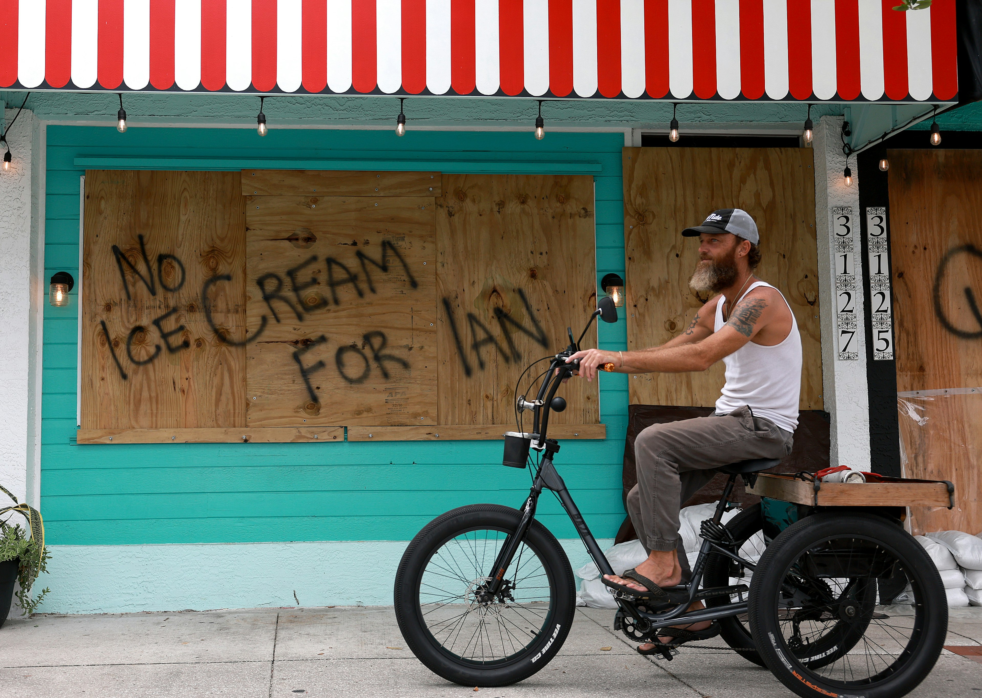 A bicyclist rides past a sign reading, 'No Ice Cream for Ian,' painted on a building that is boarded up for the possible arrival of Hurricane Ian