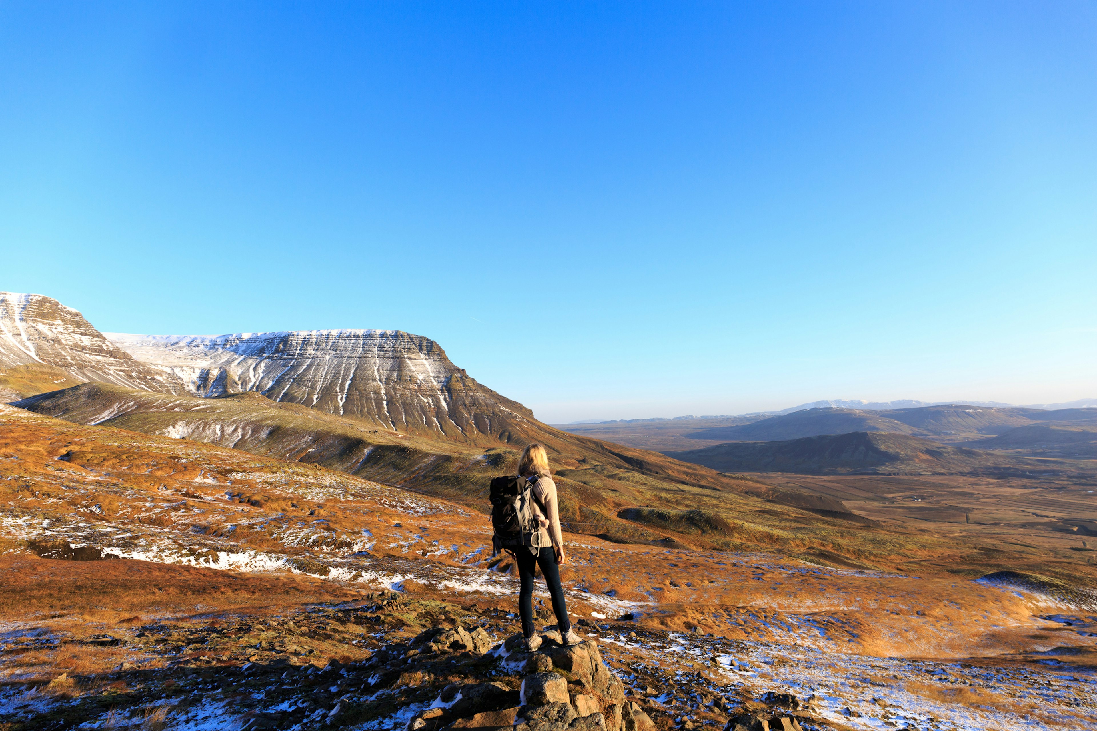 A hiker looks over the view towards a mountain in a snowy landscape