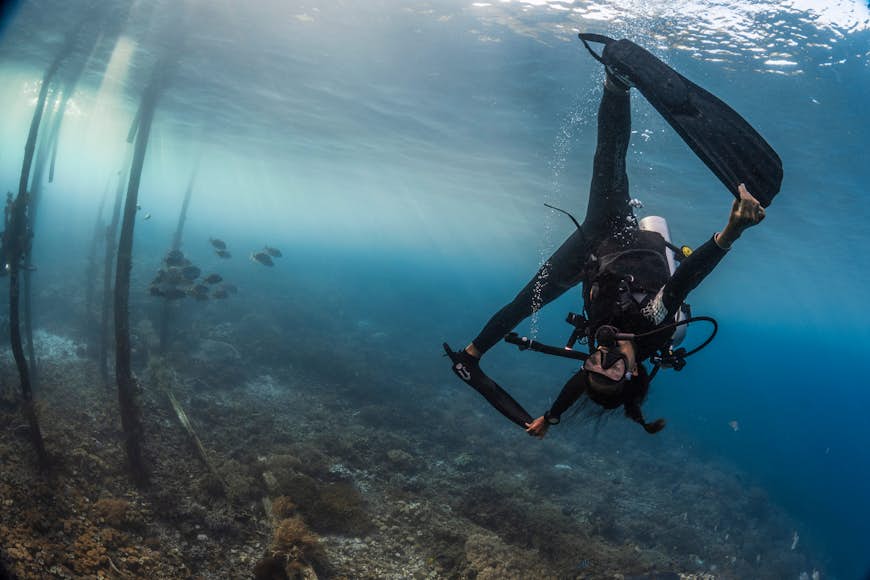 A scuba diver holding her fins as she turns upside down near the bottom of the ocean