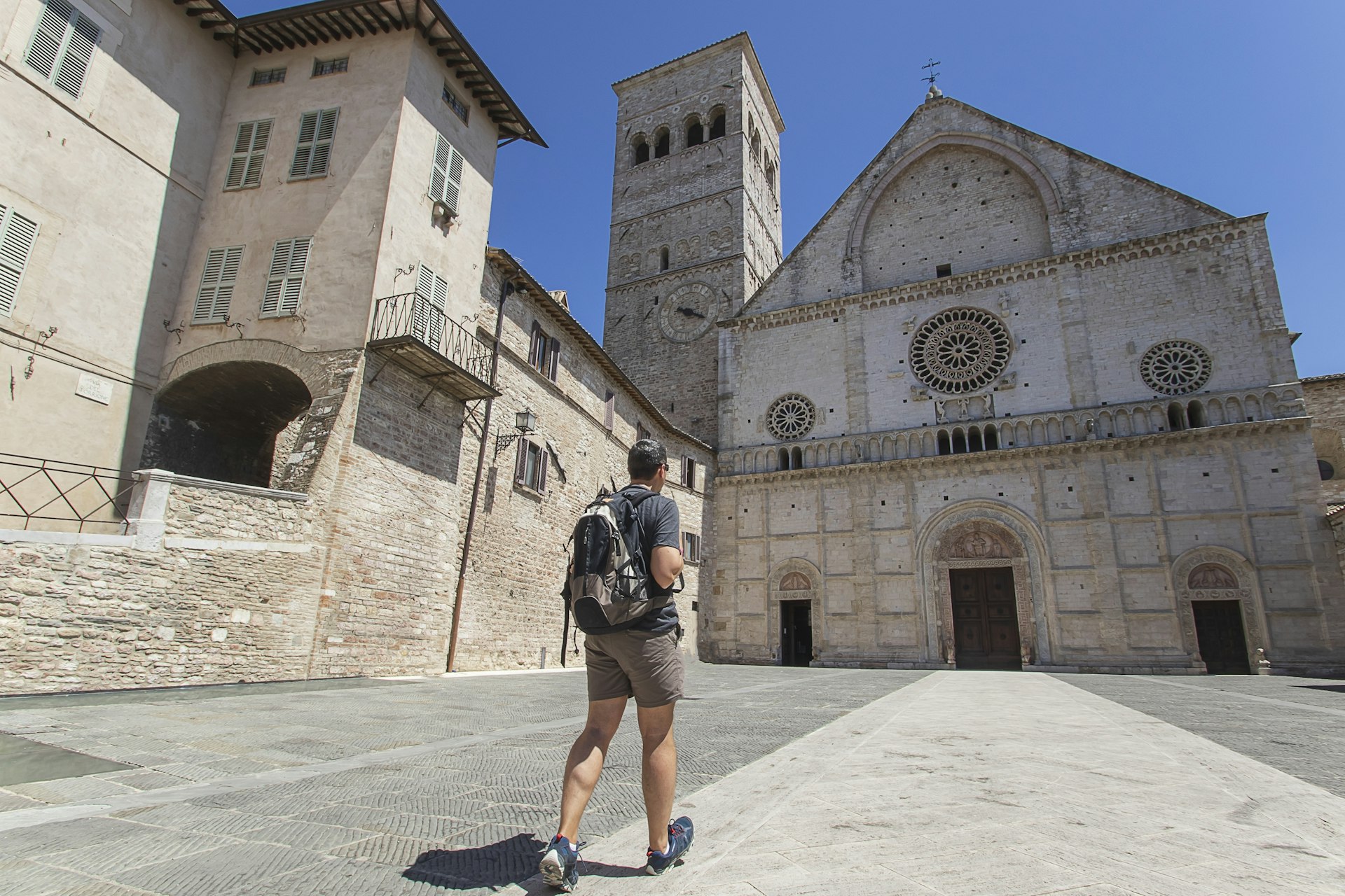 A tourist walks across an empty courtyard in front of the San Rufino Cathedral in Assisi, Italy