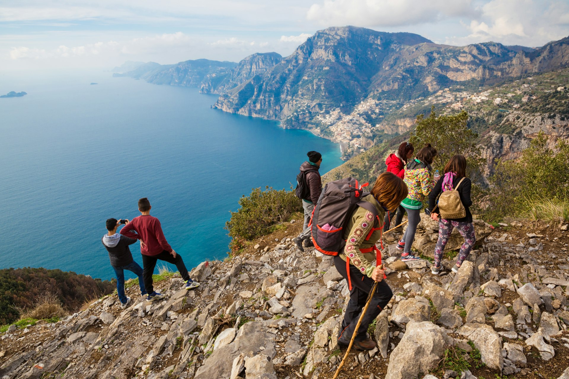 A group of friends standing on the edge of a cliff and taking photos of the coastline below on the Path of the Gods in Campania, Italy