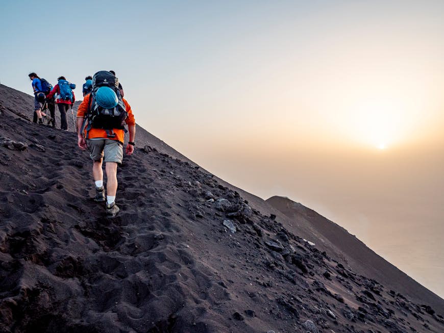ikers walking at sunset on Stromboli volcano, Aeolian Islands, Sicily, Italy. Ash and volcanic rock are the landscape of this climb.