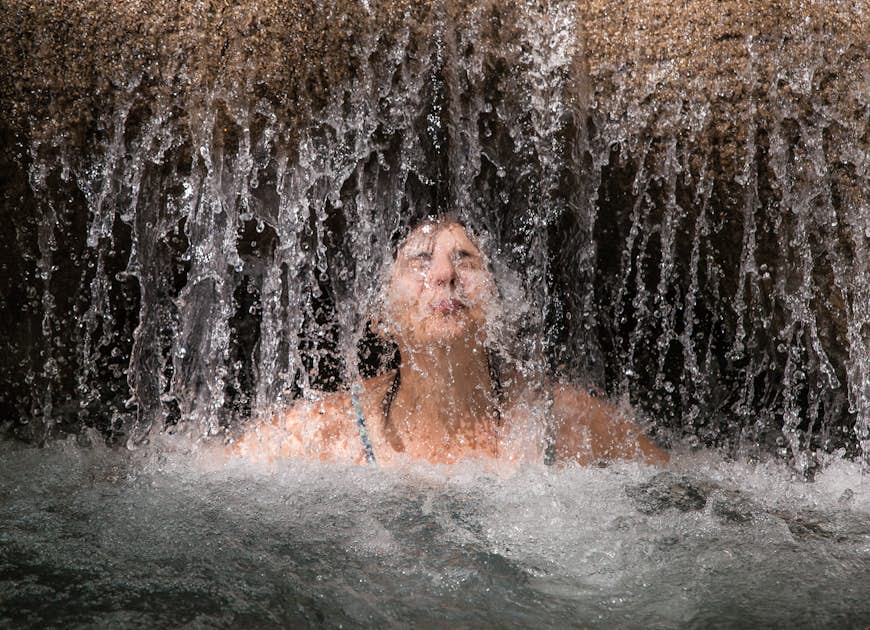 Woman enjoys a refreshing water massage at Mayfield Falls, Glenbrook, Jamaica