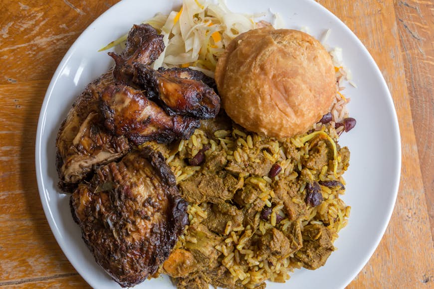 An overview of a plate of Jamaican curry goat, jerk chicken and fried dumpling