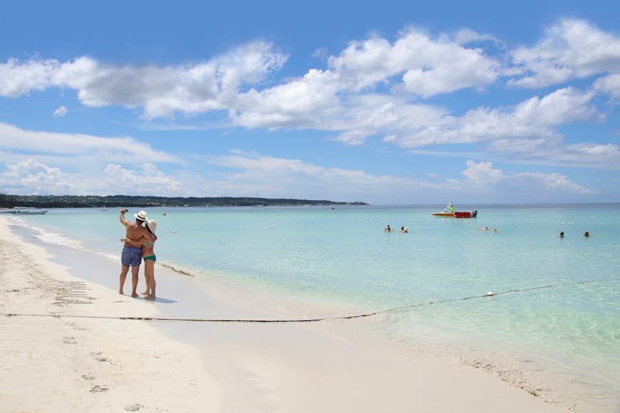Distant view of two people taking a selfie on Negril Beach while others swim in the water