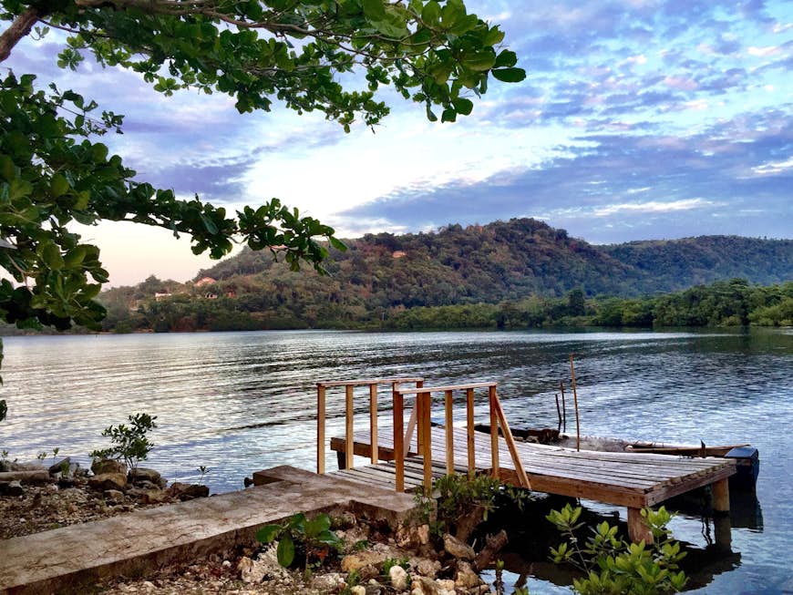 A small dock on a beautiful lake in Port Antonio Jamaica, with a mountain in the background, at sunset