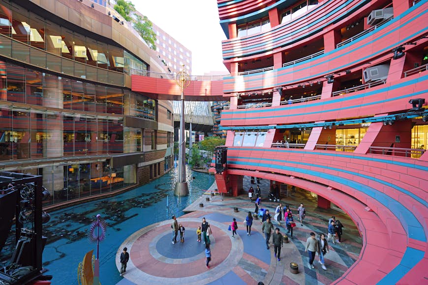 The curved pink-and-blue facade of a shopping center with people wandering below next to a canal