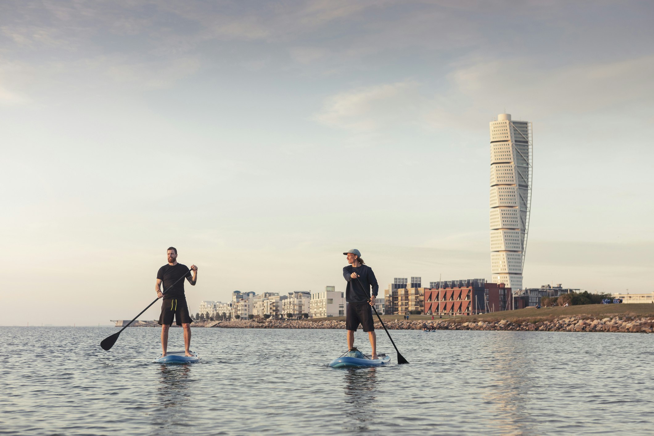 Two friends paddle boarding in front of the Turning Torso tower