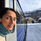 Woman looks out of train window while traveling through a snowy landscape.