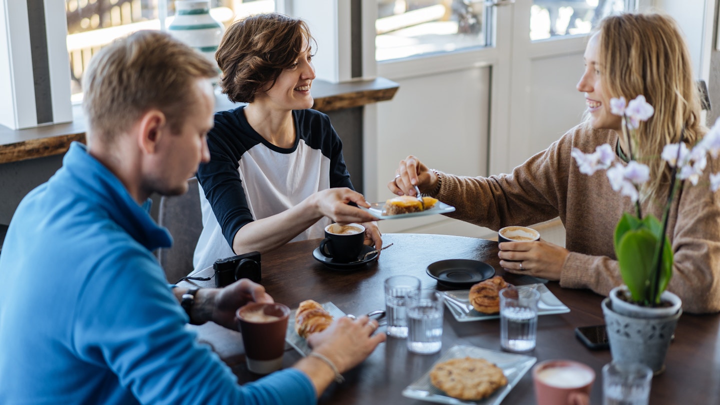 Group of cheerful women and man chatting happily while enjoying breakfast meal in cafe, Norway, Lofoten islands


