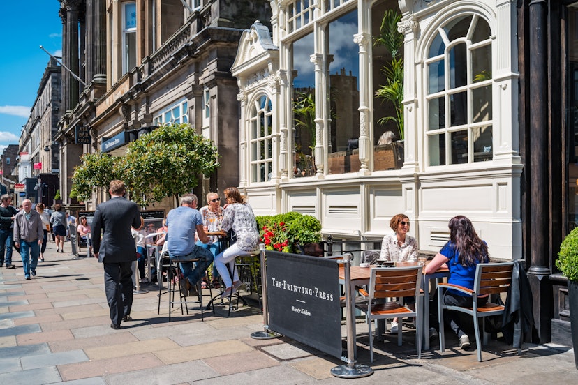 People enjoy a restaurant patio in downtown in Edinburgh, Scotland, UK on a sunny day.