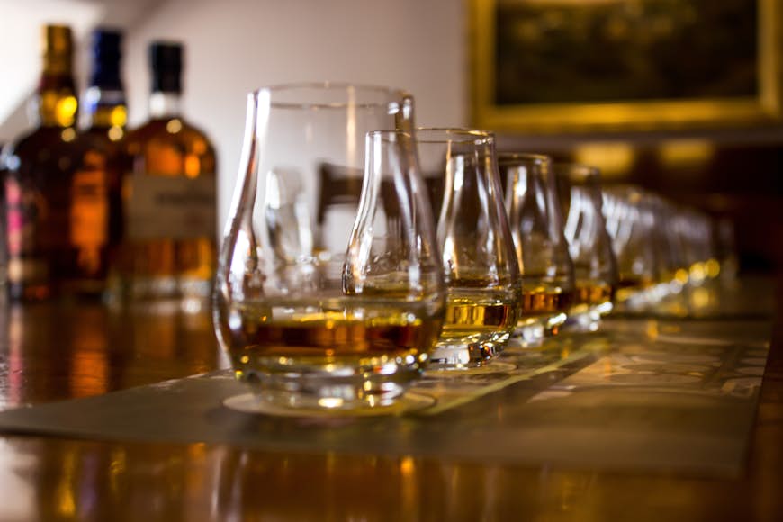 A line of tasting glasses filled with different types of Whiskies for tasting, with the focus on the second glass, the rest is out of focus