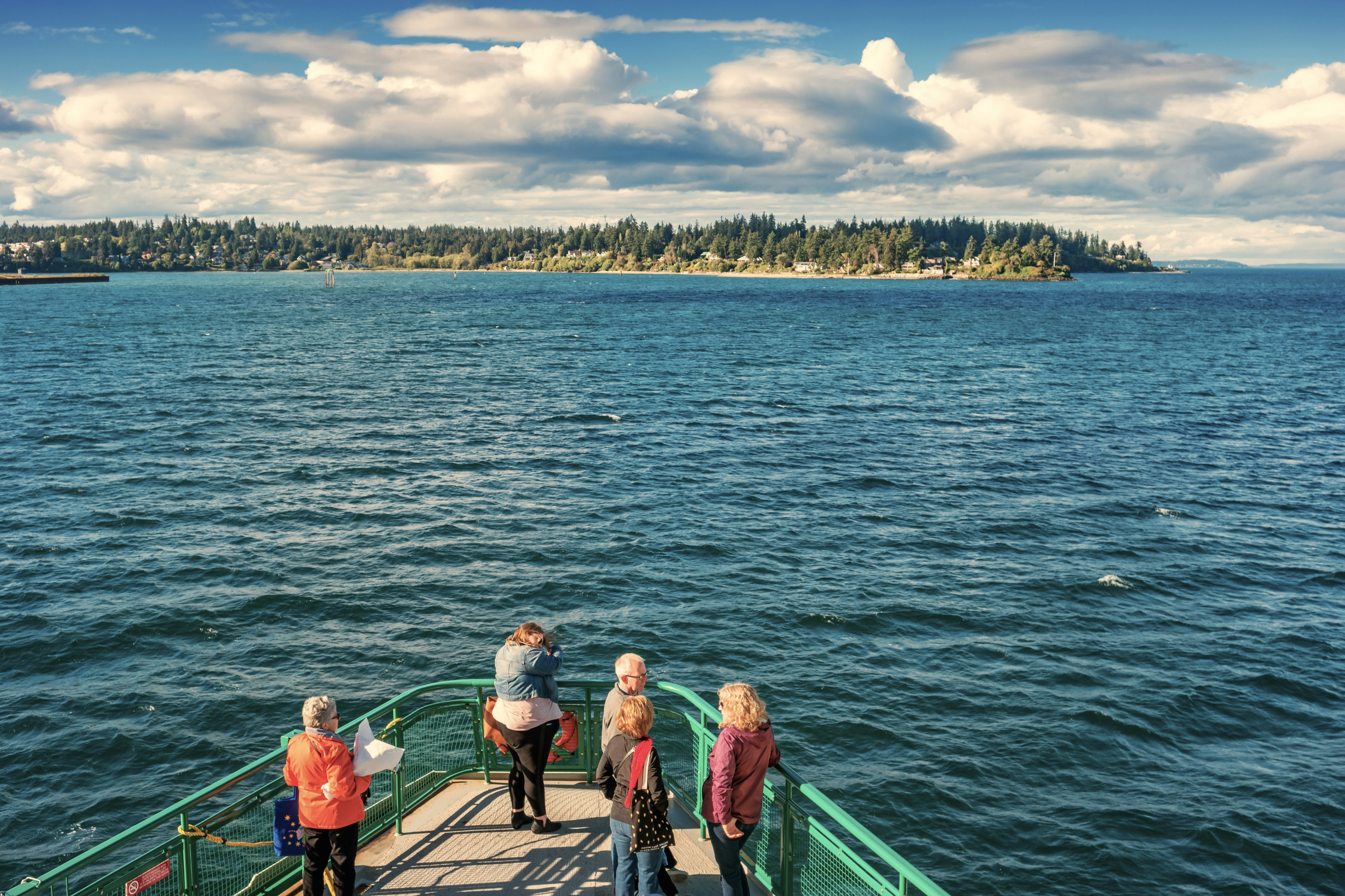 People stand on the deck of a ferry as it approaches Bainbridge Island