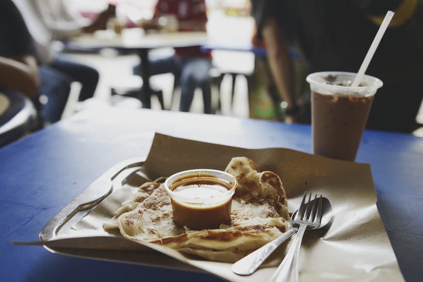 Classic Singaporean breakfast combination of roti prata and ice Milo (mal chocolate drink) with fish curry sauce at a hawker centre