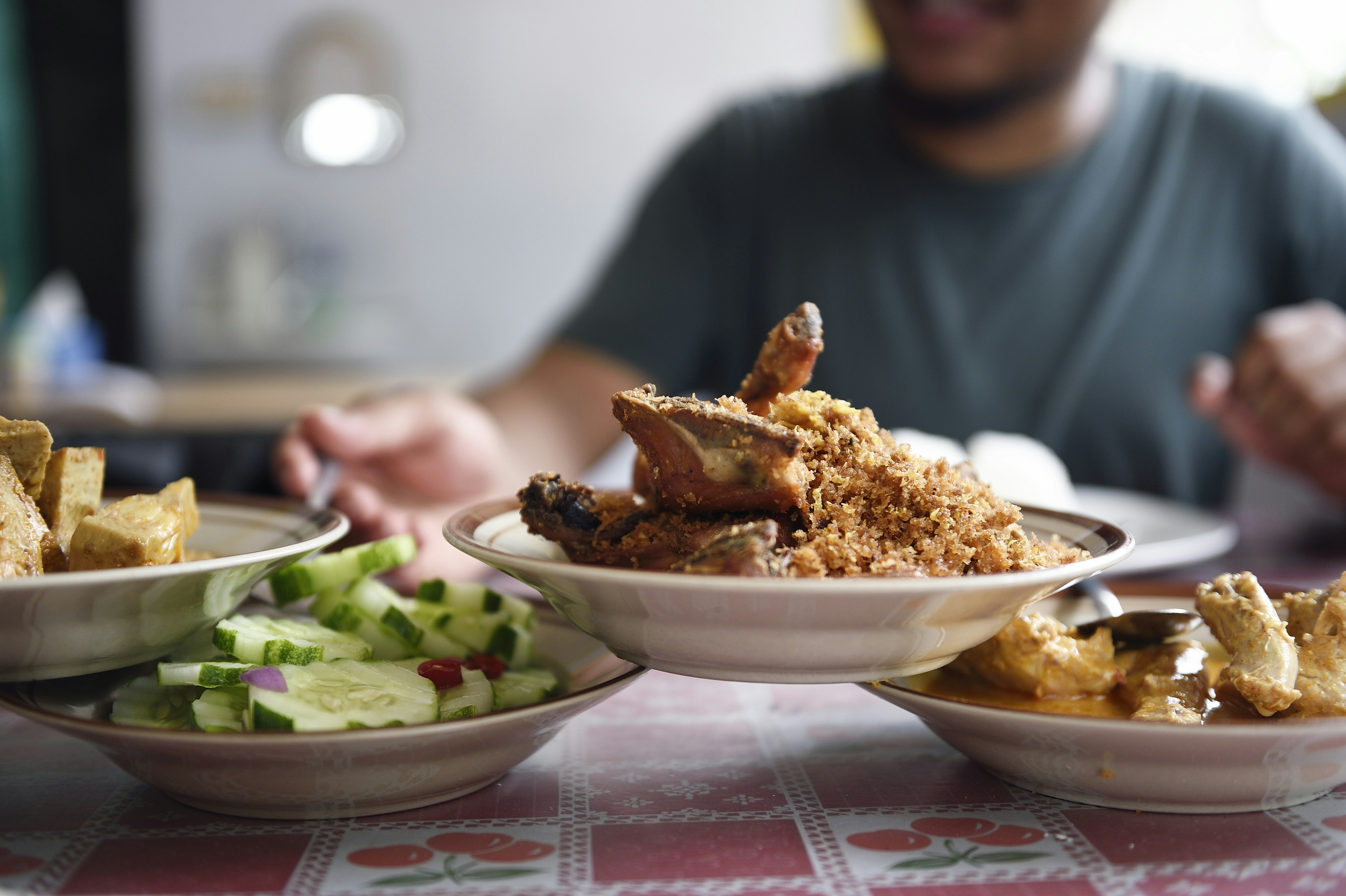 Hand reaching for a stack of Nasi Padang dishes from a street vendor