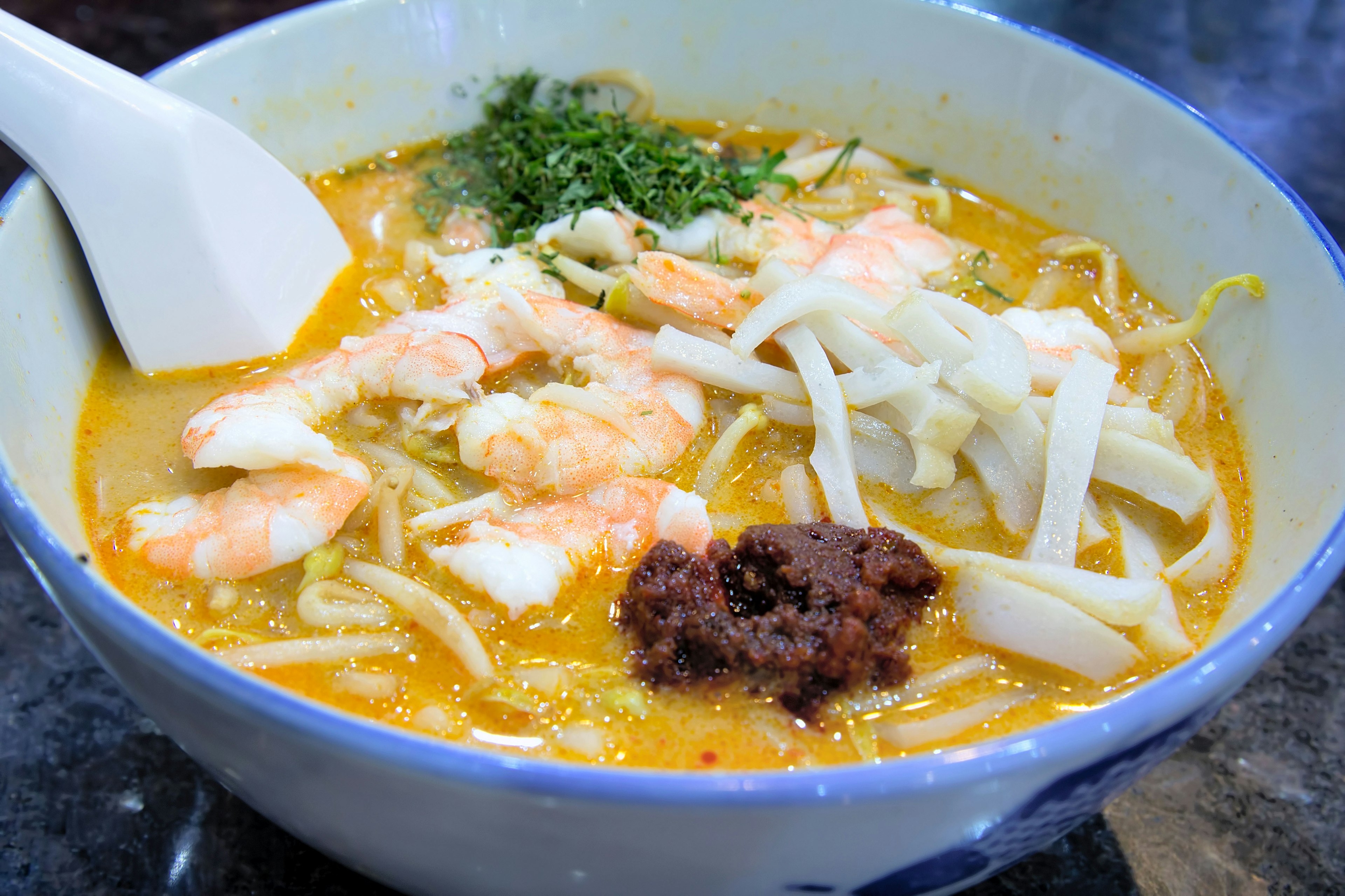 Singapore Curry Laksa with Prawns Fishcake and Sambal Chili Paste Garnished with Daun Kesom Leaves Macro