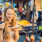 Young woman tourist eating Typical Korean street food on a walking street of Seoul. Spicy fast food simply found at local Korean martket, Soul Korea.