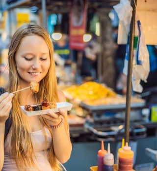 Young woman tourist eating Typical Korean street food on a walking street of Seoul. Spicy fast food simply found at local Korean martket, Soul Korea.