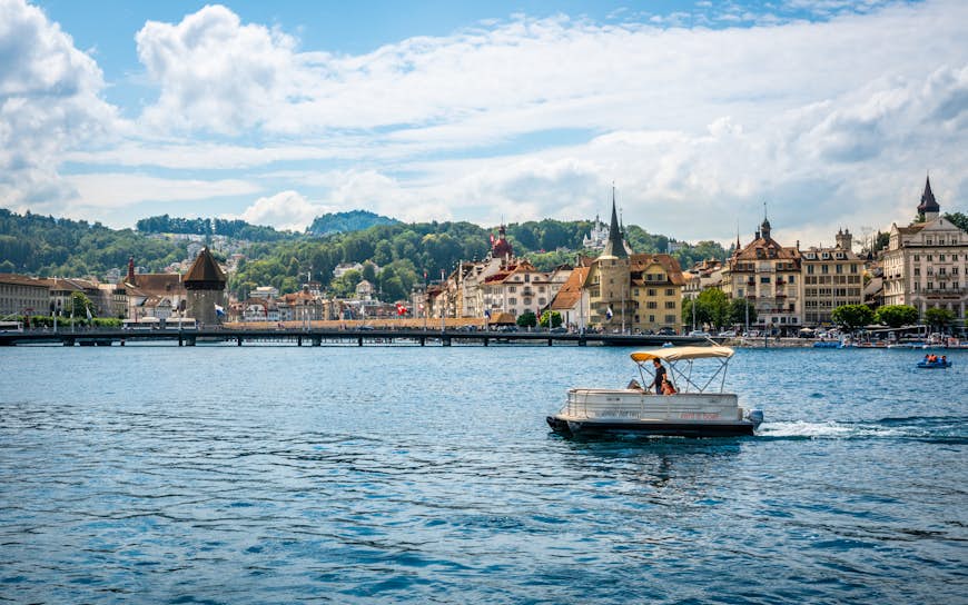 Tourists on a license free boat to rent on Lucerne lake and city with landmarks such as chapel bridge in background in Lucerne old town Switzerland