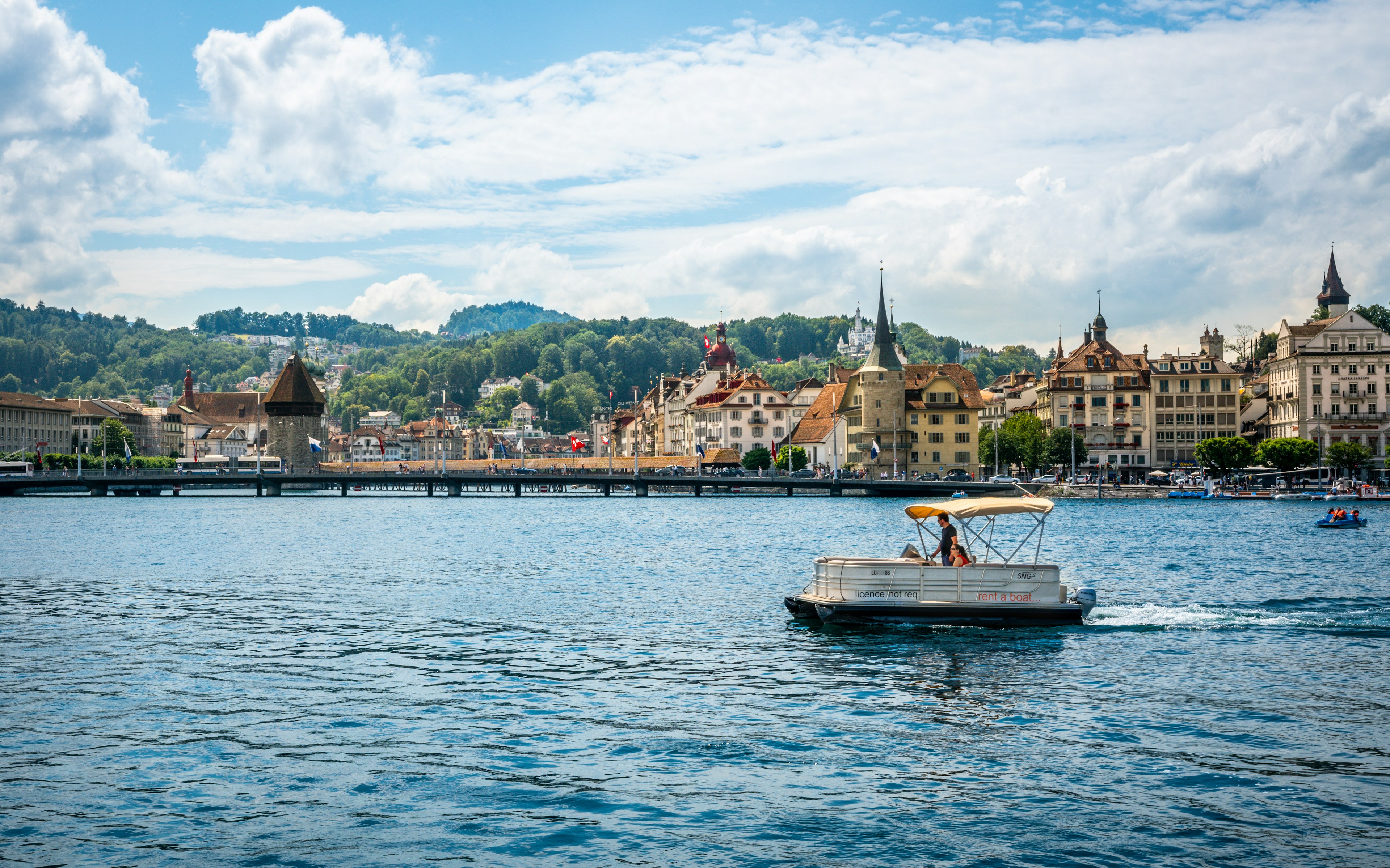 Two people take a small boat out on a lake at the edge of a scenic city