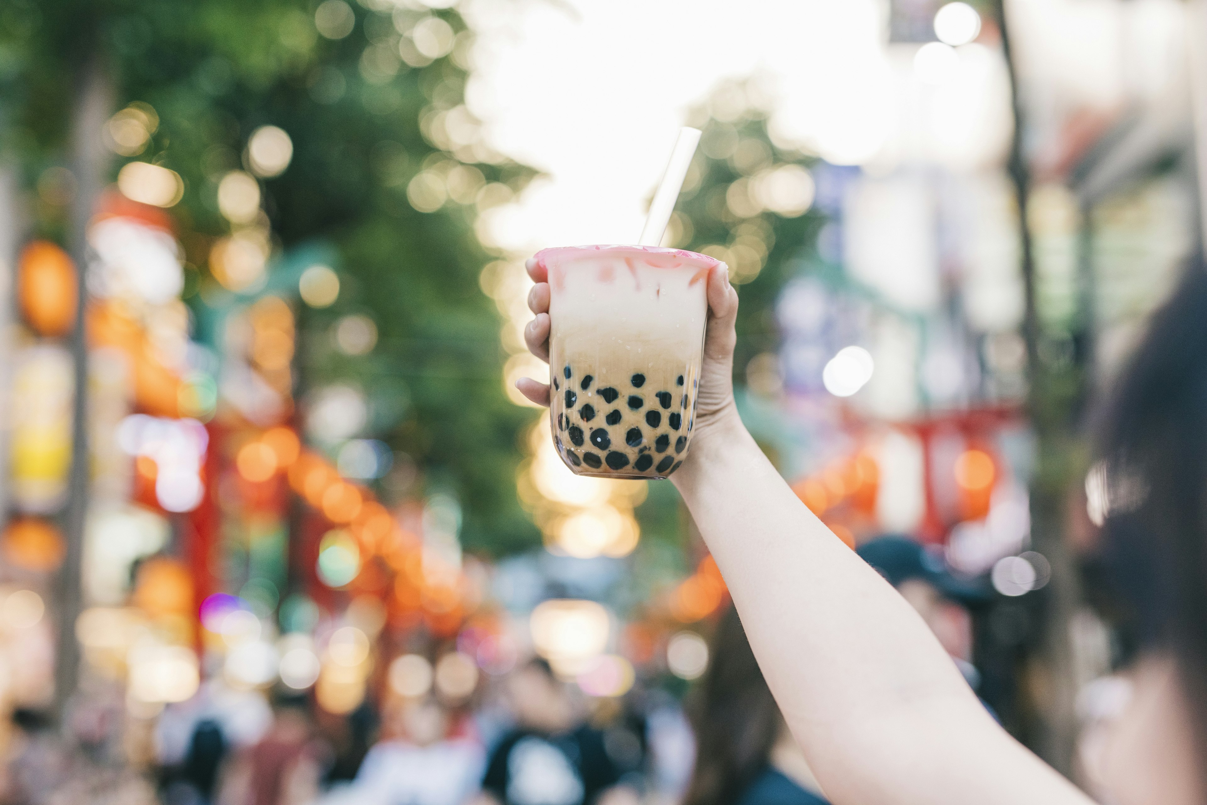 A hand holds a brown bubble tea aloft