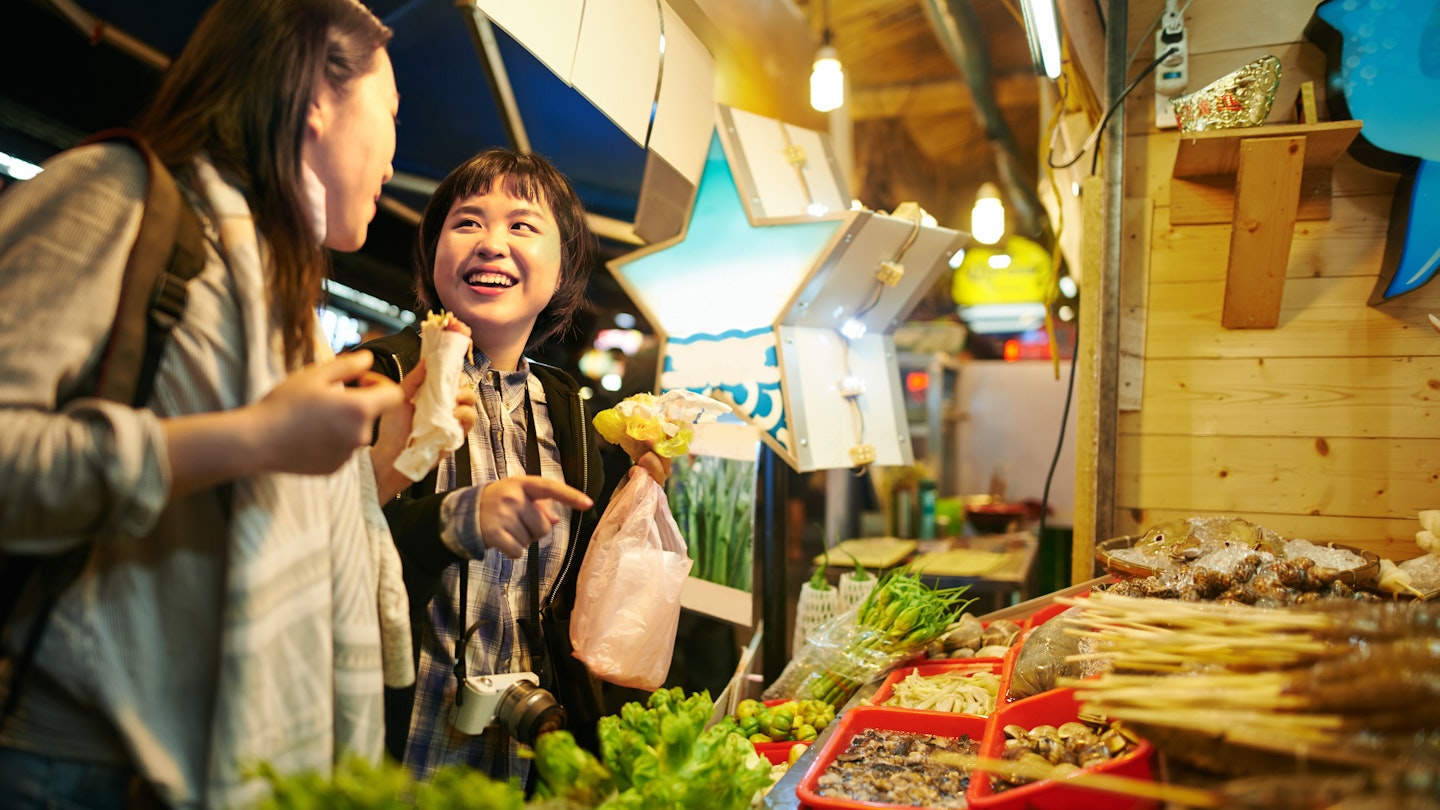 Shot of two young women eating food at a Taiwanese night market