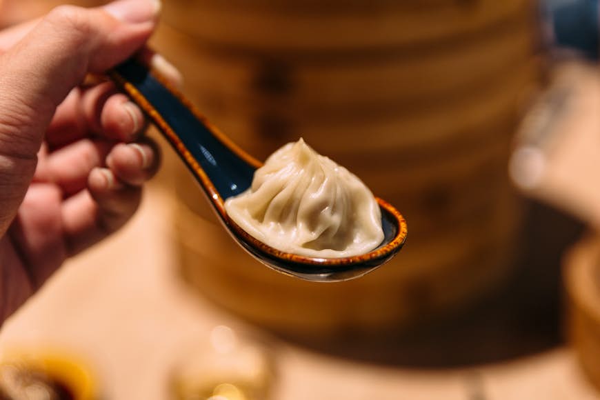 Xiao Long Bao (Soup Dumpling) in spoon with blur bamboo streamer basket in background