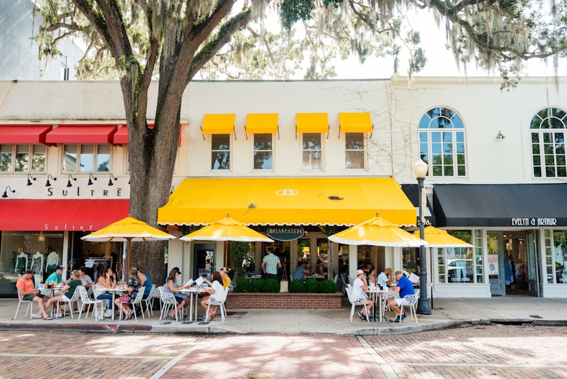 This is a horizontal, color photograph Park Avenue in downtown Winter Park, Florida. People dine at outside tables under umbrellas by the sidewalk.