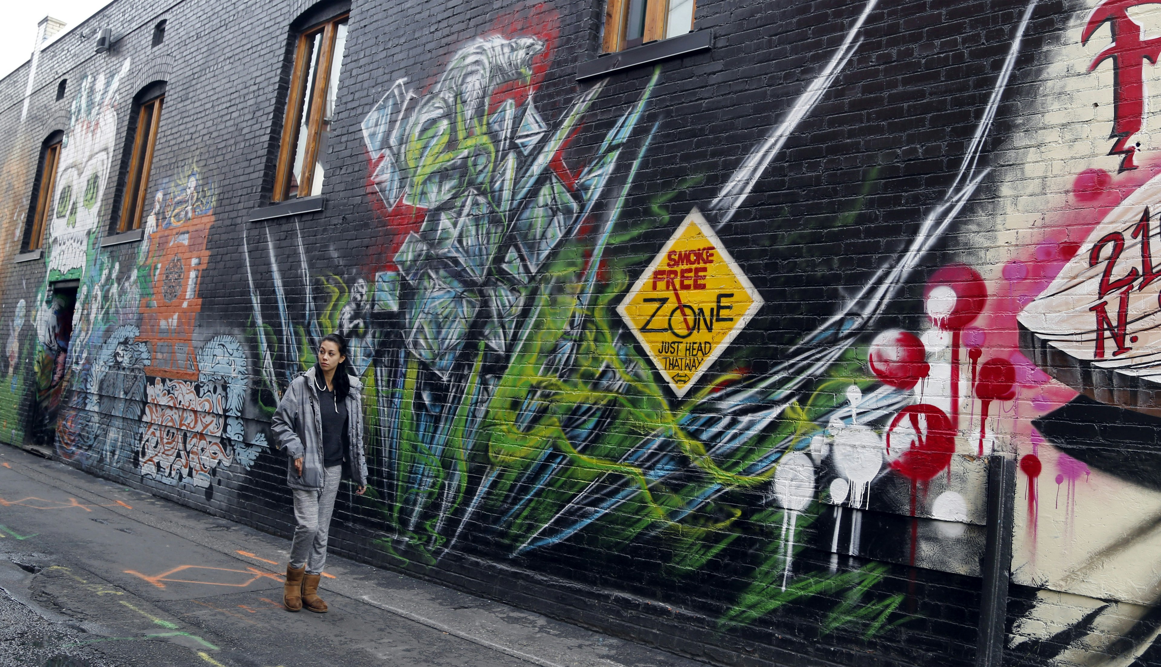 A woman walks in front of a giant outdoor mural on a black brick wall