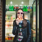 Happy young woman in sunglasses eating a slice of pizza from corner pizza joint in downtown New York City

