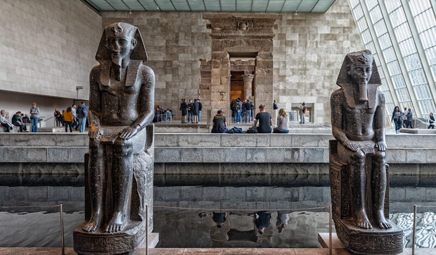 People walk around the displays of vast pharaoh sculptures in the Egyptian Temple of Dendur at the Met
