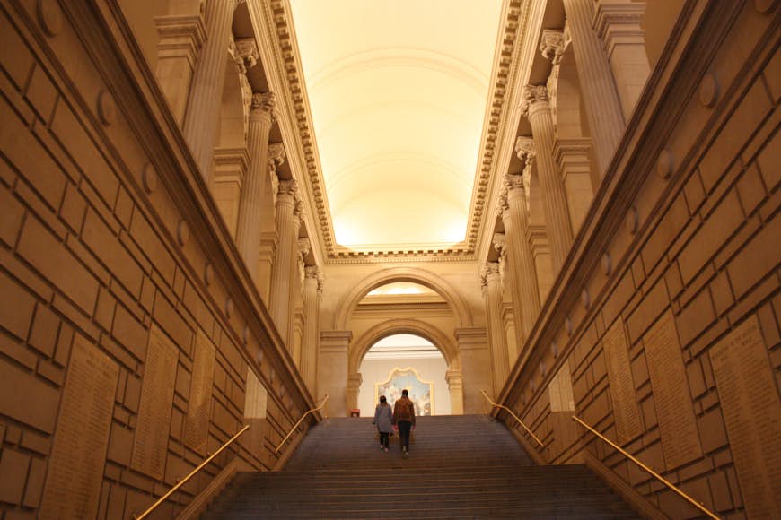 Two people walk up a staircase within a grand museum building