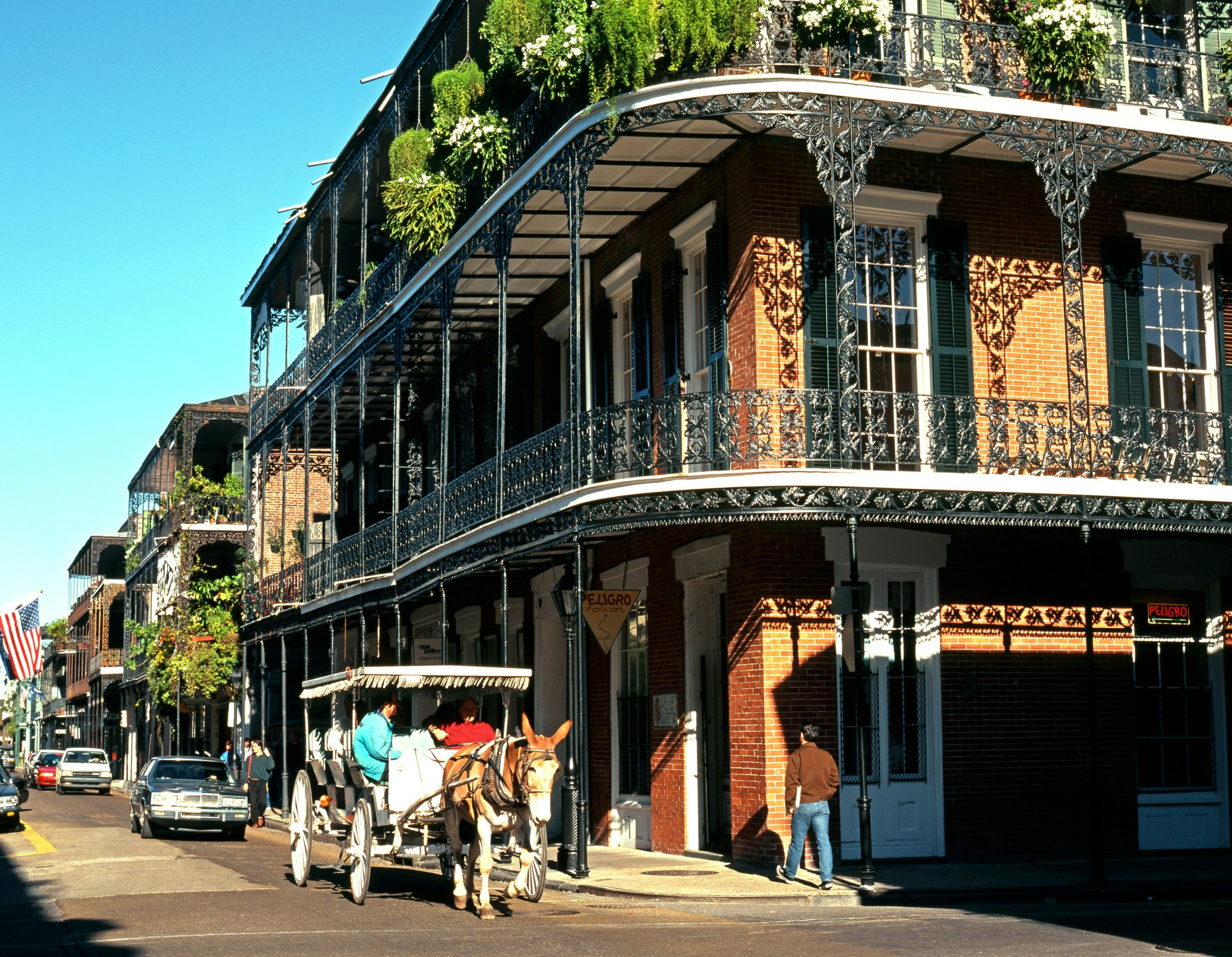 A horse-drawn carriage passes a corner building with an intricate wrought-iron wrap-around balcony