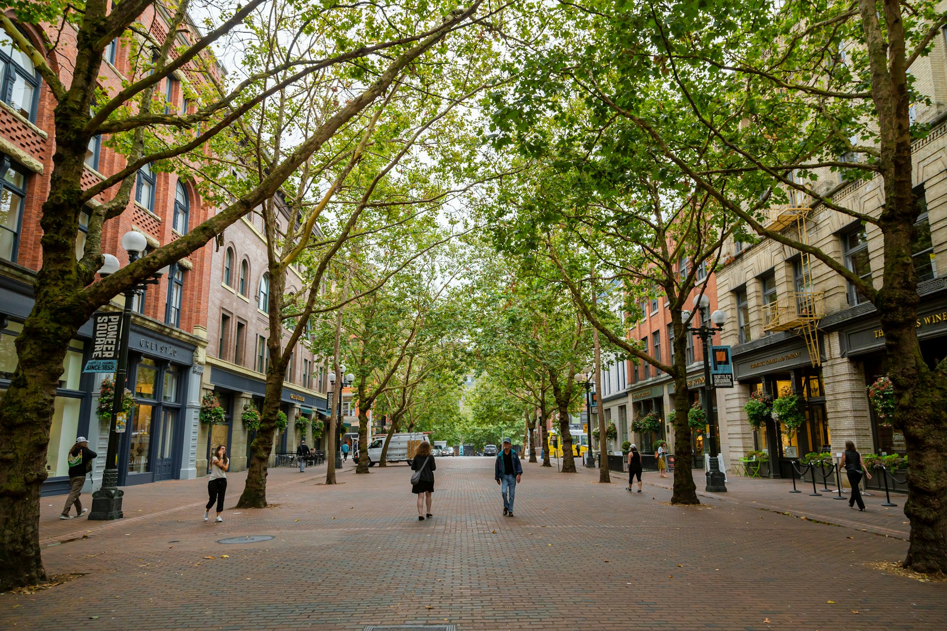 People walk on a tree-lined street on the historic brick Occidental Walk Avenue in the Pioneer Square neighborhood of Seattle, Washington