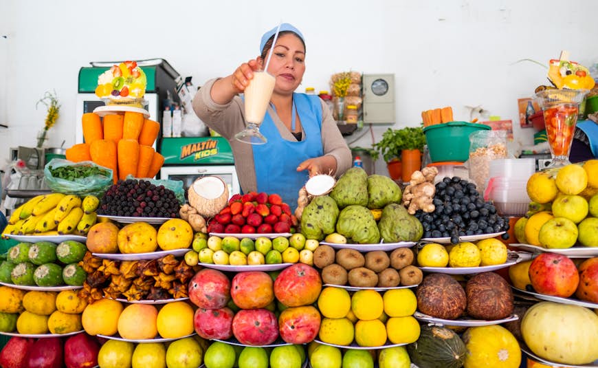 Bolivian woman gives the cup with freshly squizzed juice on the market in the city of Sucre with abundance of fruits on the foreground